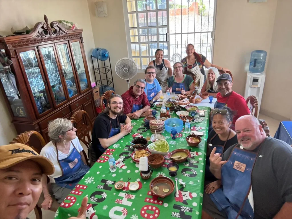A diverse group of happy travelers enjoying a meal they prepared together around a festive table during an authentic market-to-table cooking class in a local Cozumel home.