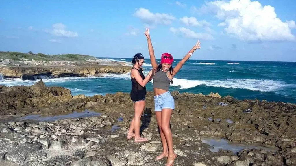 Two happy women celebrating on the rugged, rocky coastline of Cozumel's east side during an off-road adventure tour, with the blue ocean behind them.