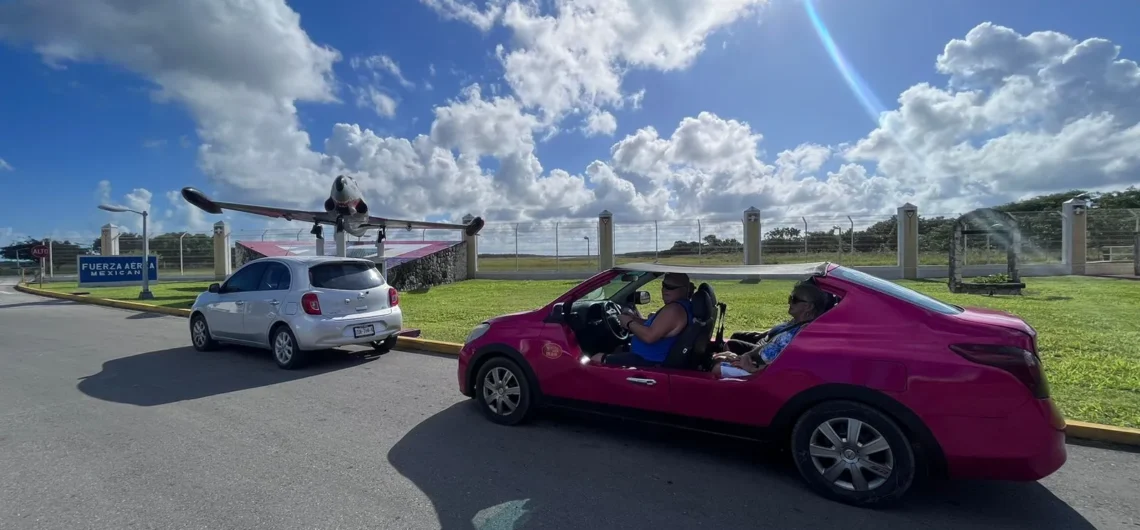 Two guests enjoying a sunny day on their Cozumel excursion, driving a bright pink convertible buggy near the air force monument.