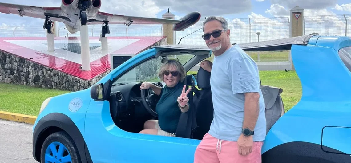 A happy couple enjoying their private Cozumel tour, posing with a bright blue buggy in front of the iconic air force fighter jet monument.