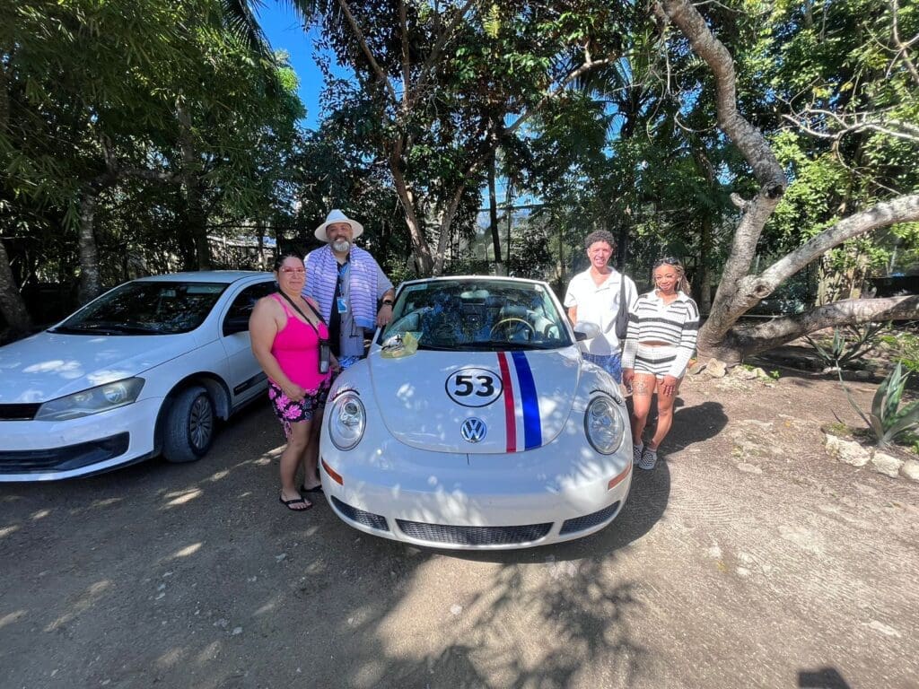A happy group of four posing with a classic white VW Beetle convertible during their unique private tour in a lush, sunny Cozumel setting.