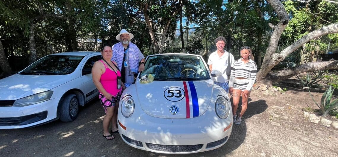 A happy group of four posing with a classic white VW Beetle convertible during their unique private tour in a lush, sunny Cozumel setting.